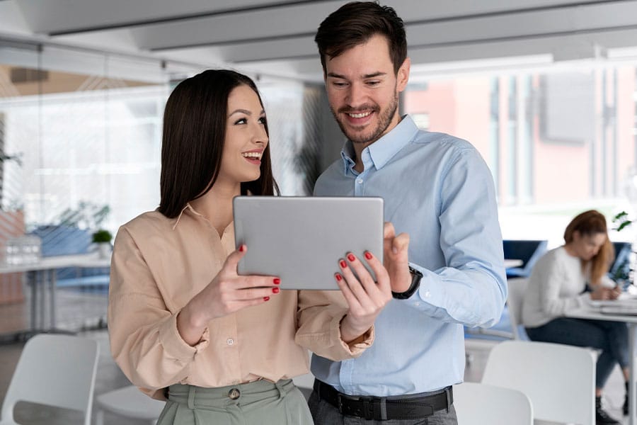 Smiling woman and man discussing property transaction details on a tablet in a modern office setting, reflecting The Title Haus's commitment to seamless real estate services.