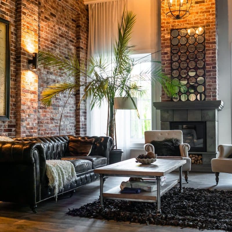 Cozy living room featuring a black leather chesterfield sofa, a wooden coffee table, decorative plants, and a brick wall, emphasizing a stylish and inviting home environment relevant to title services in Florida real estate transactions.