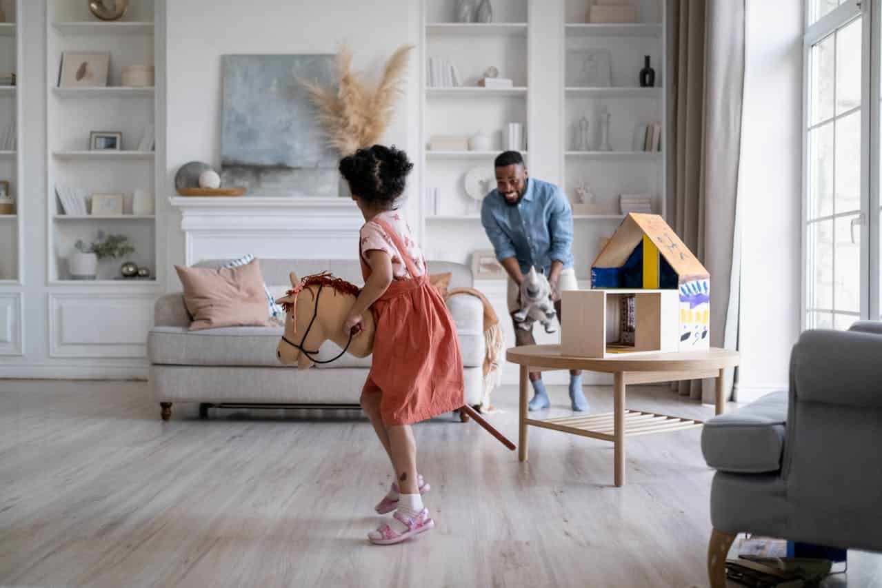 Child playing with a toy horse in a bright living room, while an adult smiles and holds a stuffed animal, emphasizing family bonding and playtime.