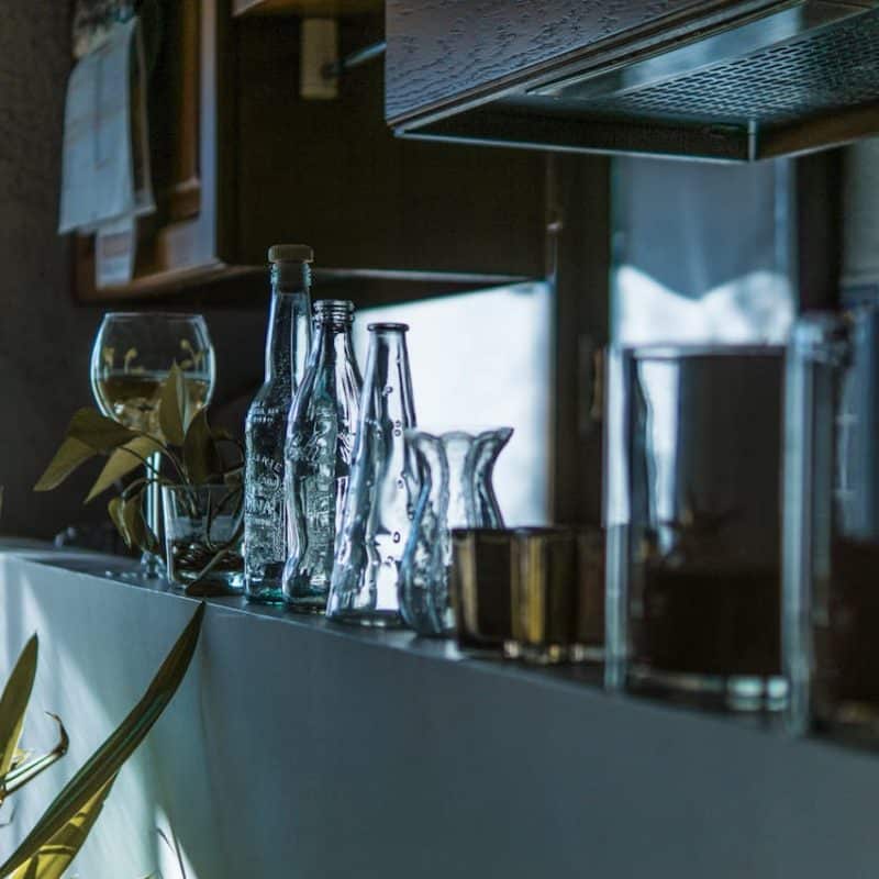 Collection of glass bottles and vases on a kitchen countertop, with natural light highlighting their shapes and reflections.