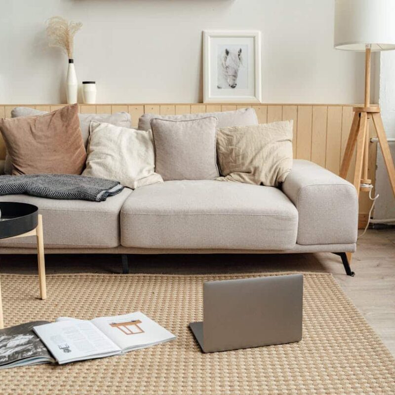 Cozy living room setting with a light-colored sofa adorned with various pillows, a laptop on the floor, and open magazines, reflecting a comfortable home environment for discussions on title services and real estate processes.