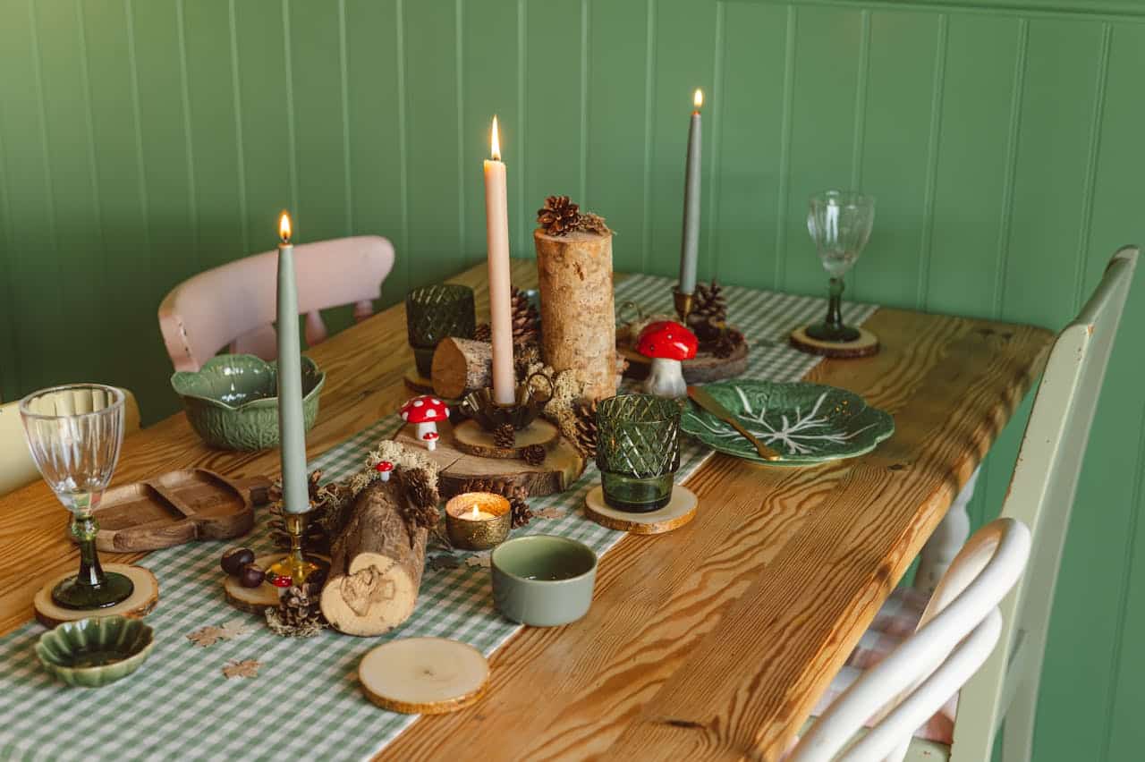 Decorative dining table with candles, pinecones, and rustic elements, featuring green and red accents, suitable for a cozy gathering or holiday setting.