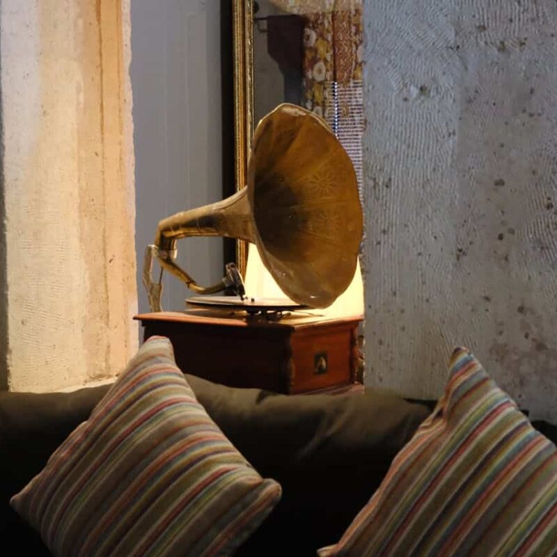 Antique gramophone on a wooden table beside striped cushions in a cozy interior setting.