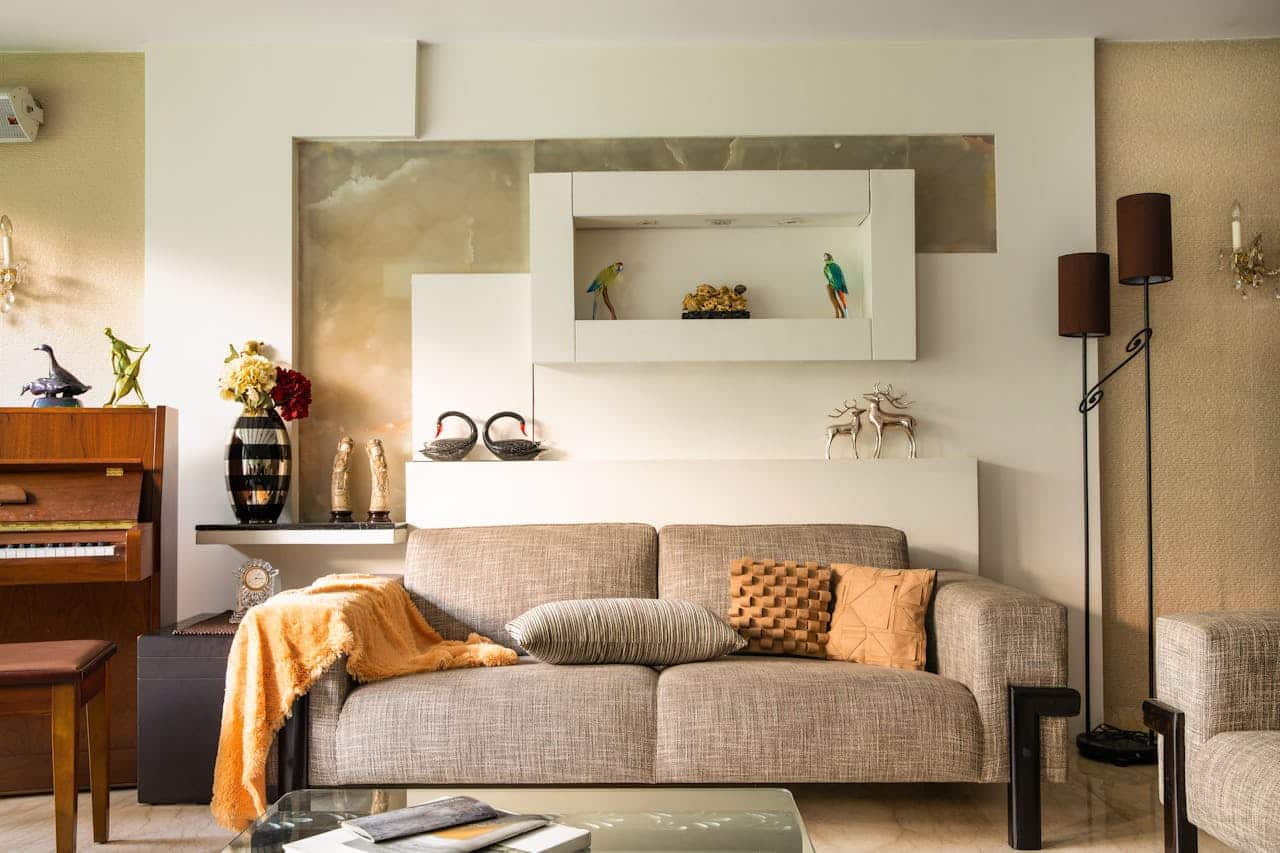 Cozy living room featuring a gray sofa with decorative pillows, an orange throw blanket, a wooden piano, and a shelf displaying decorative items, emphasizing a welcoming atmosphere for real estate discussions.