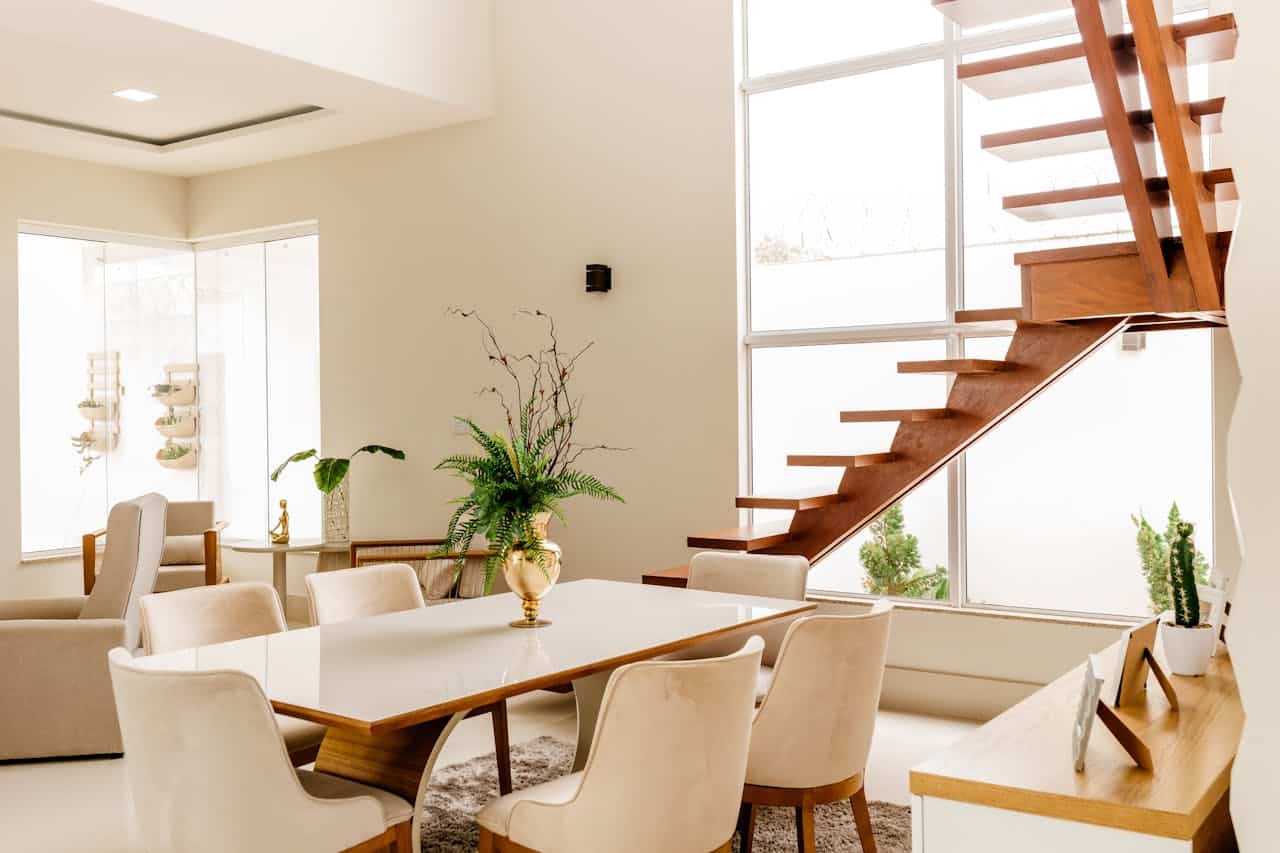 Modern interior of a dining area with a wooden staircase, featuring a glass wall, elegant dining table, plush chairs, and decorative plants, relevant to title insurance discussions in Florida real estate.